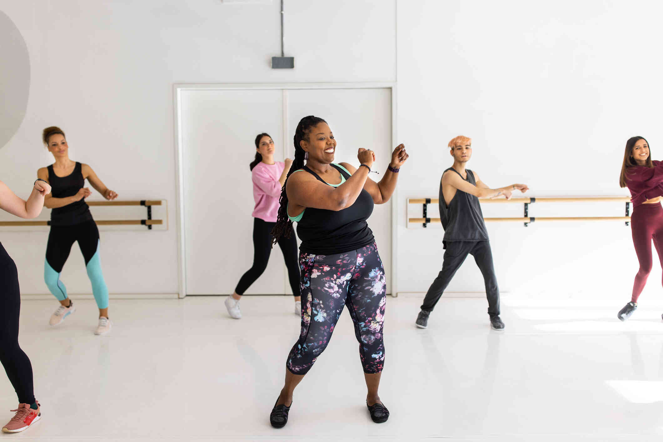 A group of women in workout clothes smiles as they take a dance class in a fitness studio and move their arms.